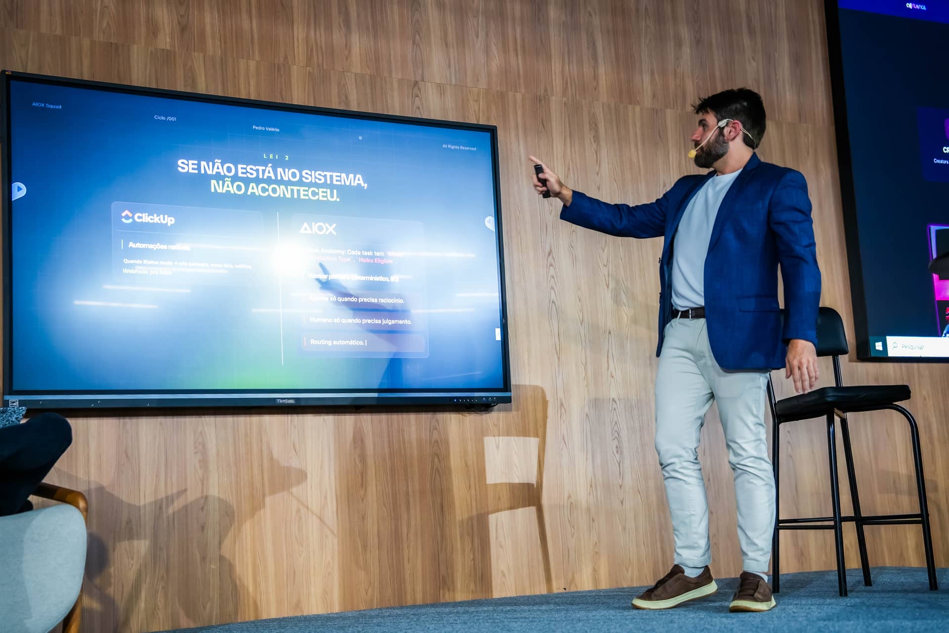 Pedro Valério no palco da imersão AIOX, apontando para o telão com a Lei 2 do método: se não está no sistema, não aconteceu
